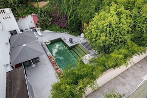 A rooftop swimming pool with a small deck area, surrounded by lush greenery and a white building.