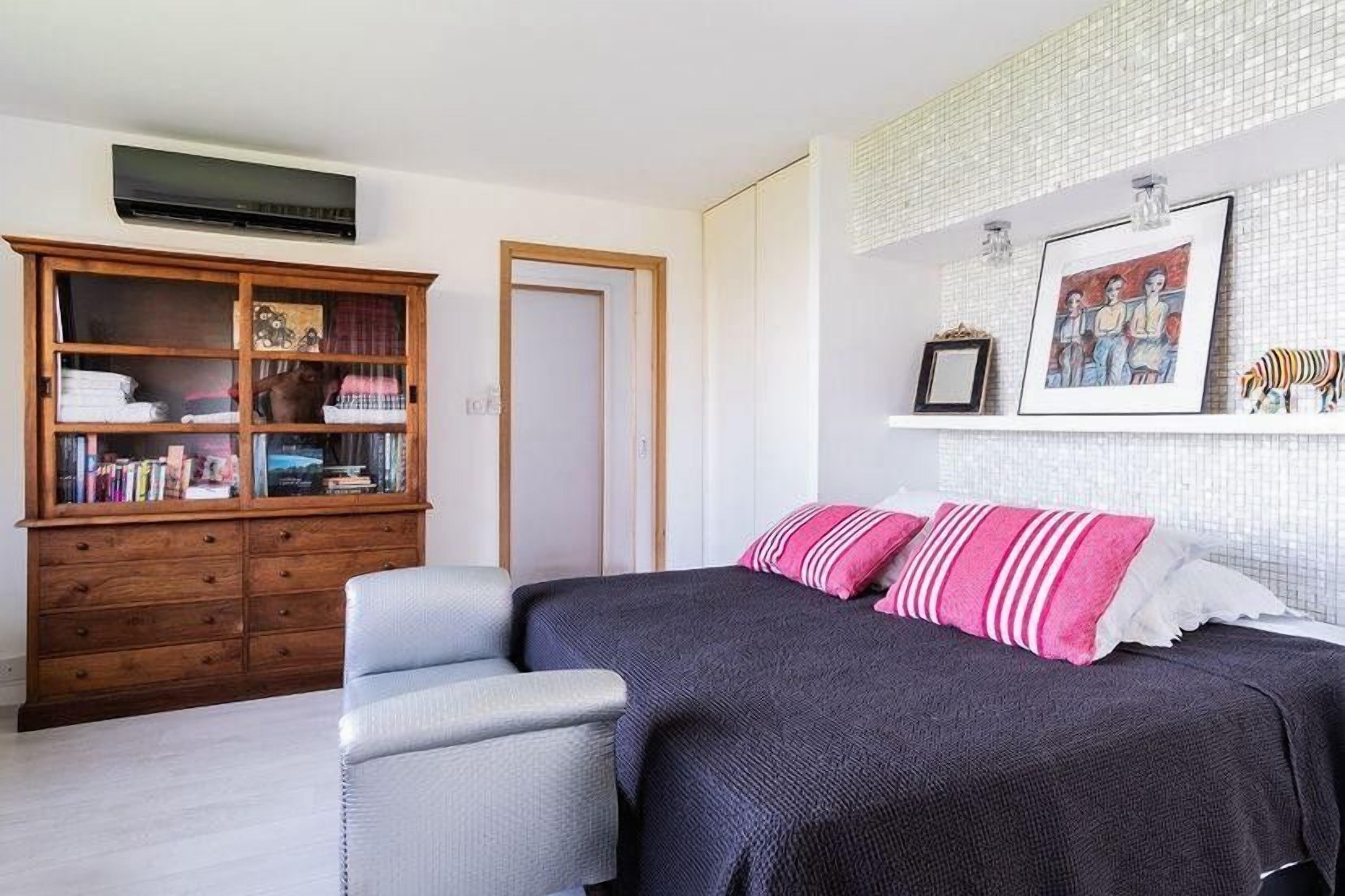 Une chambre à coucher avec un lit, une table de chevet, une armoire en bois et un mur blanc orné d’un tableau.