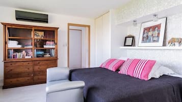 Une chambre à coucher avec un lit, une table de chevet, une armoire en bois et un mur blanc orné d’un tableau.