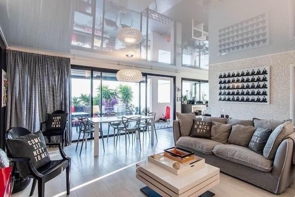 A modern living room with a sofa, coffee table, and a dining area with chairs and a table.