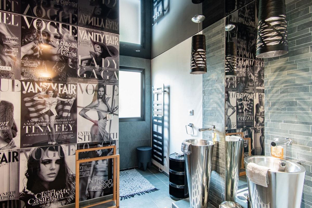 Une salle de bain moderne avec des affiches tirées de magazines, un grand miroir et un lavabo au design original.