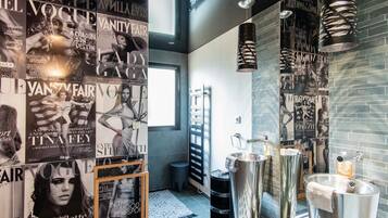 Une salle de bain moderne avec des affiches tirées de magazines, un grand miroir et un lavabo au design original.