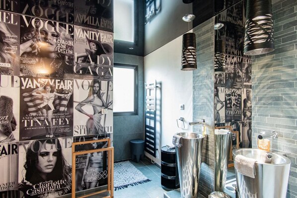 Un baño moderno con carteles de revistas, un espejo grande y un diseño de lavamanos original.