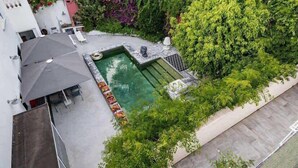 A rooftop pool with a hot tub, surrounded by lush greenery and a covered seating area.