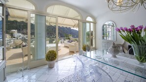 Un ampio balcone con vista chiara sulle montagne, un tavolo in vetro con sedie e un vaso di fiori.