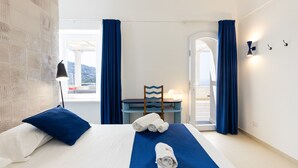 Une chambre d’hôtel avec un lit, un bureau et une chaise. Il y a des serviettes sur le lit et une lampe sur le bureau.