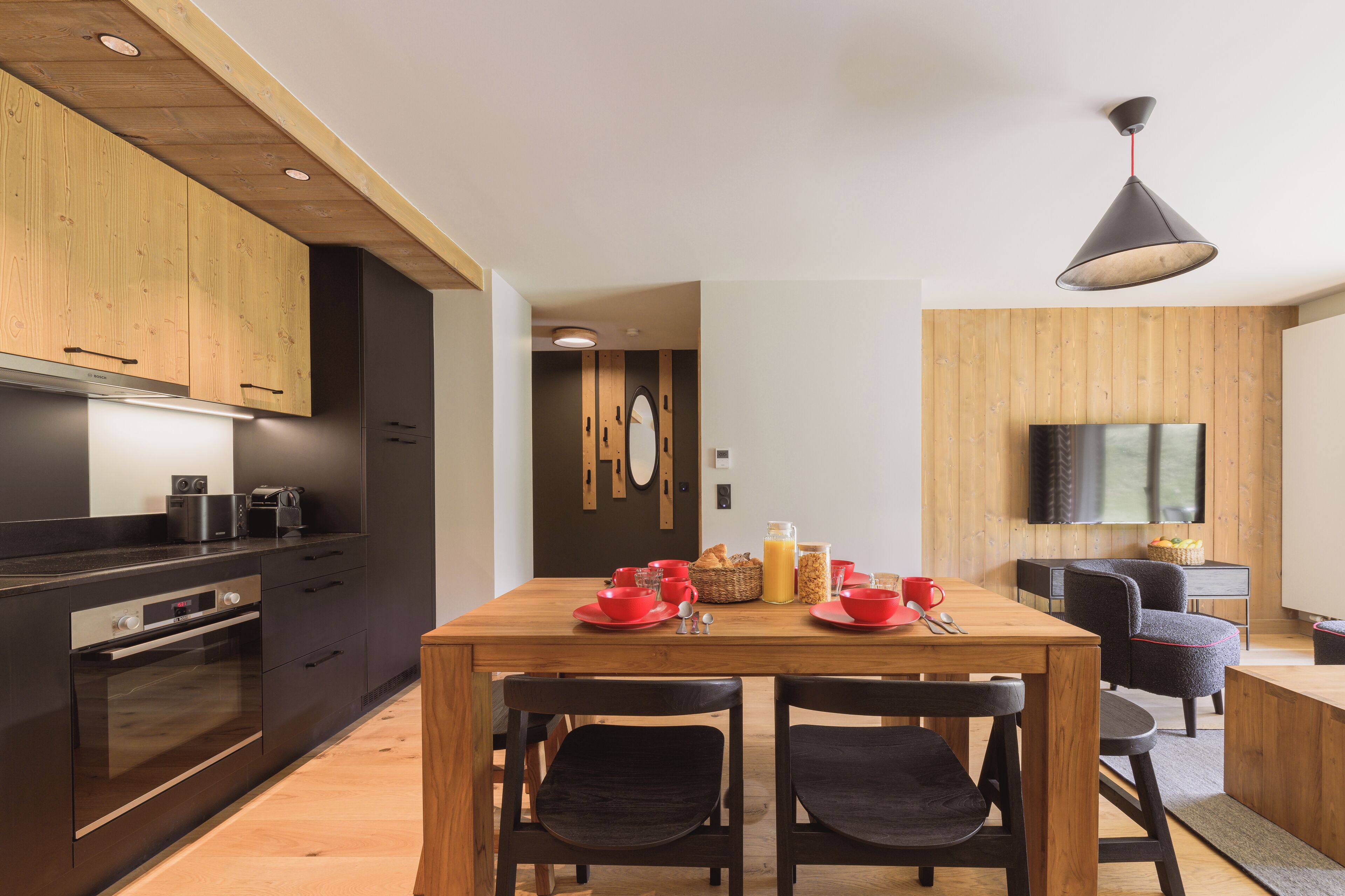 A modern kitchen with dark cabinetry, a wooden dining table, and a black pendant light.