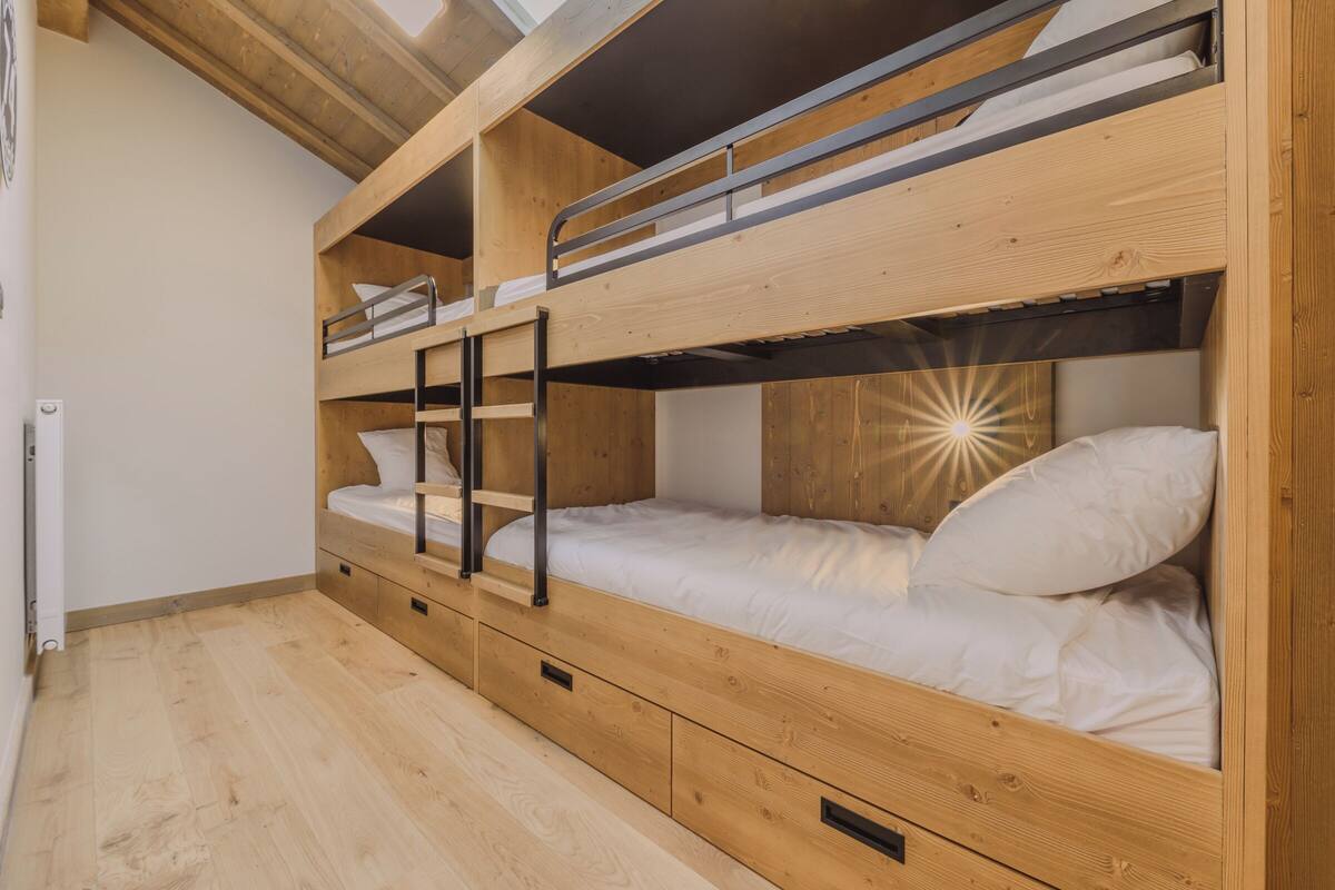 A bunk bed room with wooden walls and floors, a skylight, and a built-in desk.