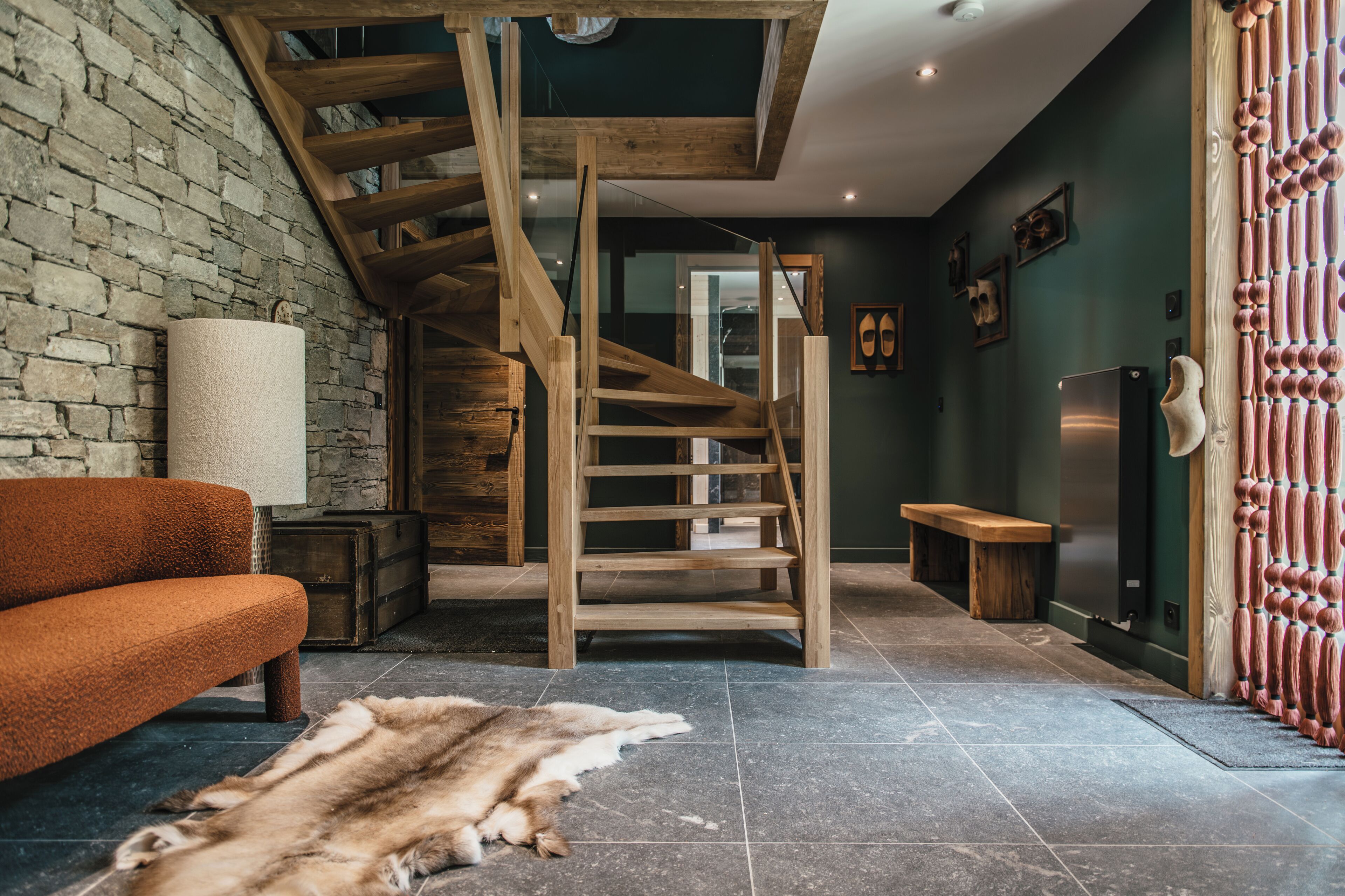 A rustic interior with a wooden staircase, a stone wall, and a leather rug.