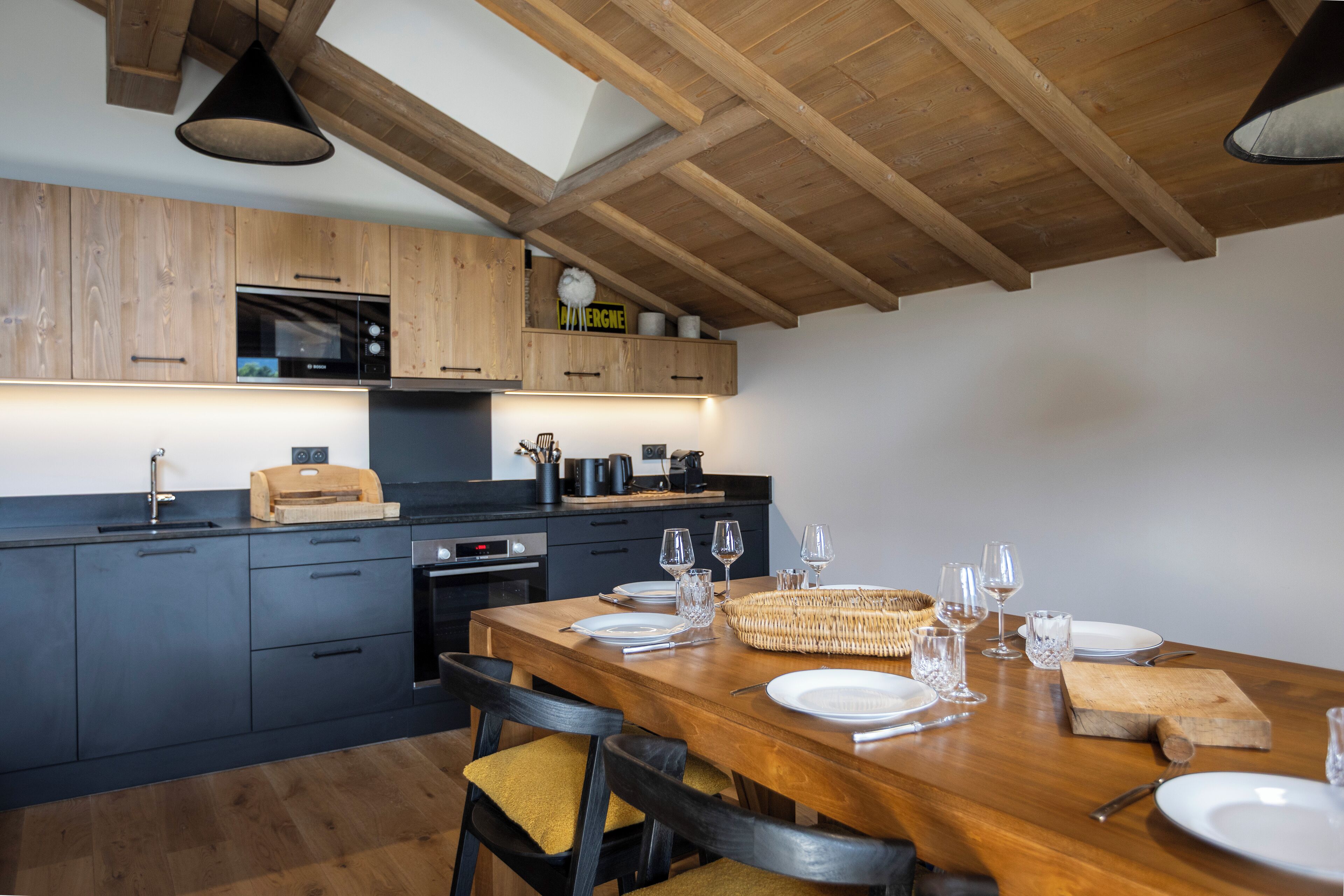 Una cocina moderna con armarios de madera, una mesa de comedor preparada para cuatro comensales y un microondas sobre la encimera.