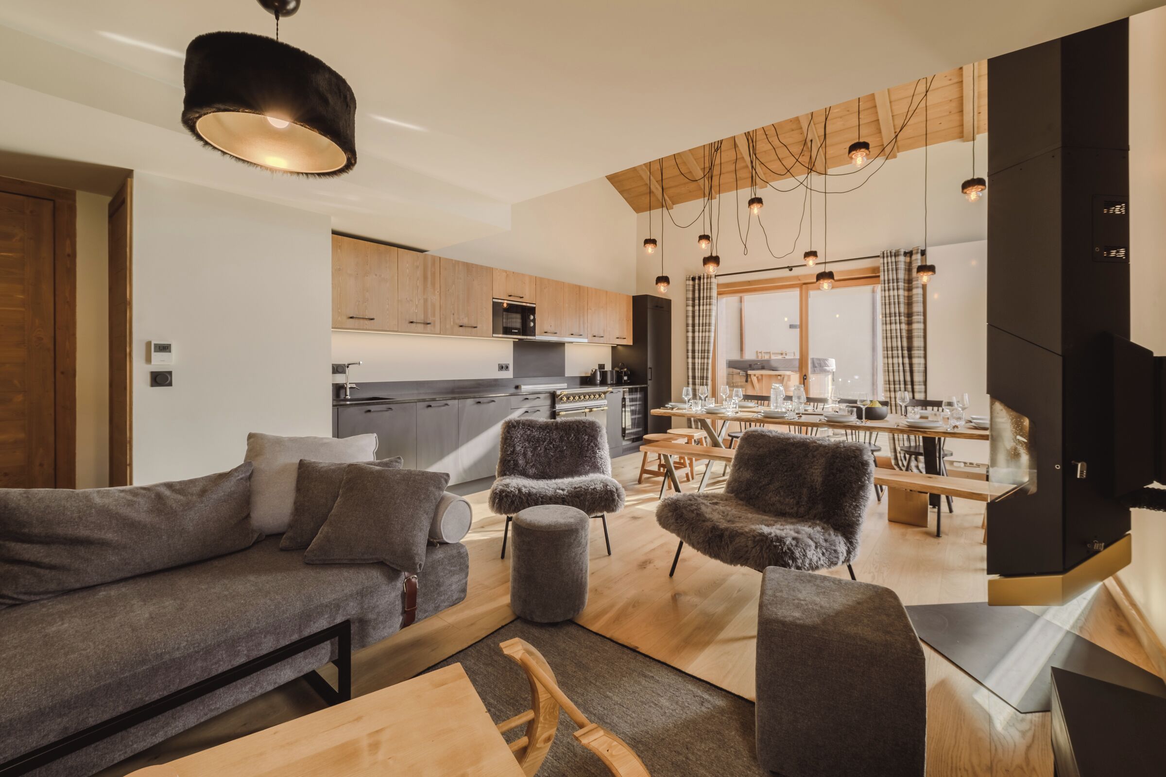 A modern living room with a sofa, ottoman, and chairs, a dining area with a table and chairs, and a kitchen with wooden cabinets and appliances.