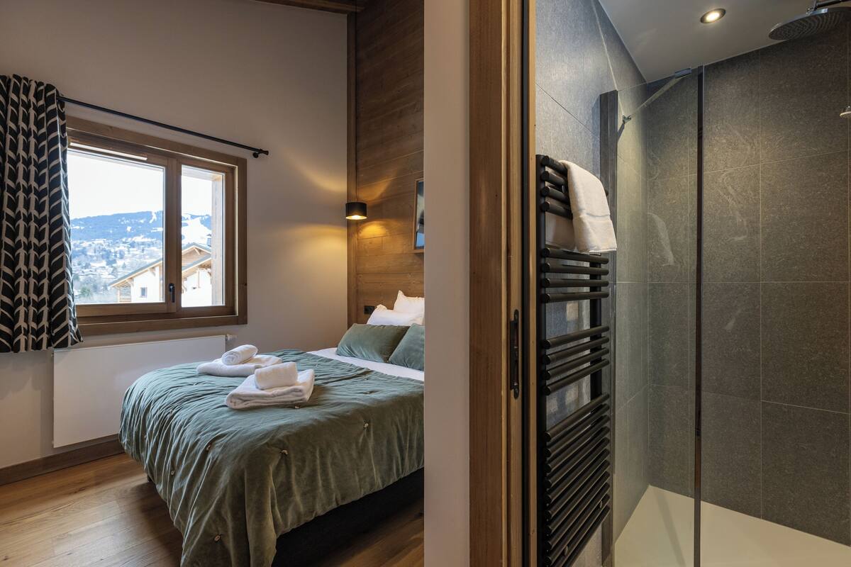 A bedroom with a bed, a window, a shower area, and a view of the outside.