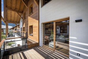 Una terraza de madera con barandilla de vidrio, una escalera de madera y vistas del paisaje circundante.