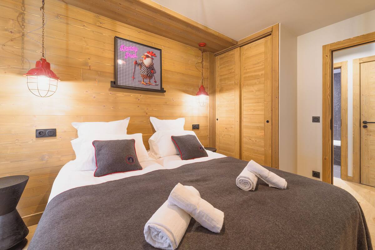 A neatly made bed with white and brown bedding, two pillows, and two rolled towels.