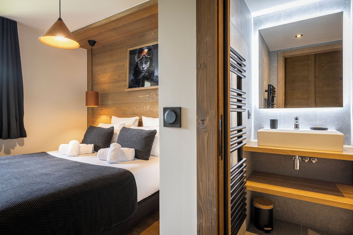 A modern hotel room with a large bed, a wooden headboard, a mounted picture, a built-in sink, and a towel rack.