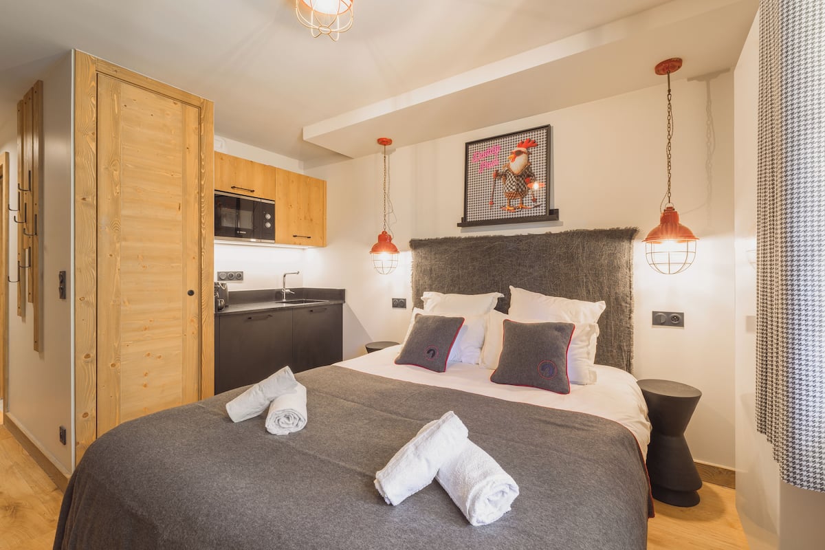 A bedroom with a bed, pillows, a headboard, a wall-mounted artwork, and a kitchen area with a microwave.