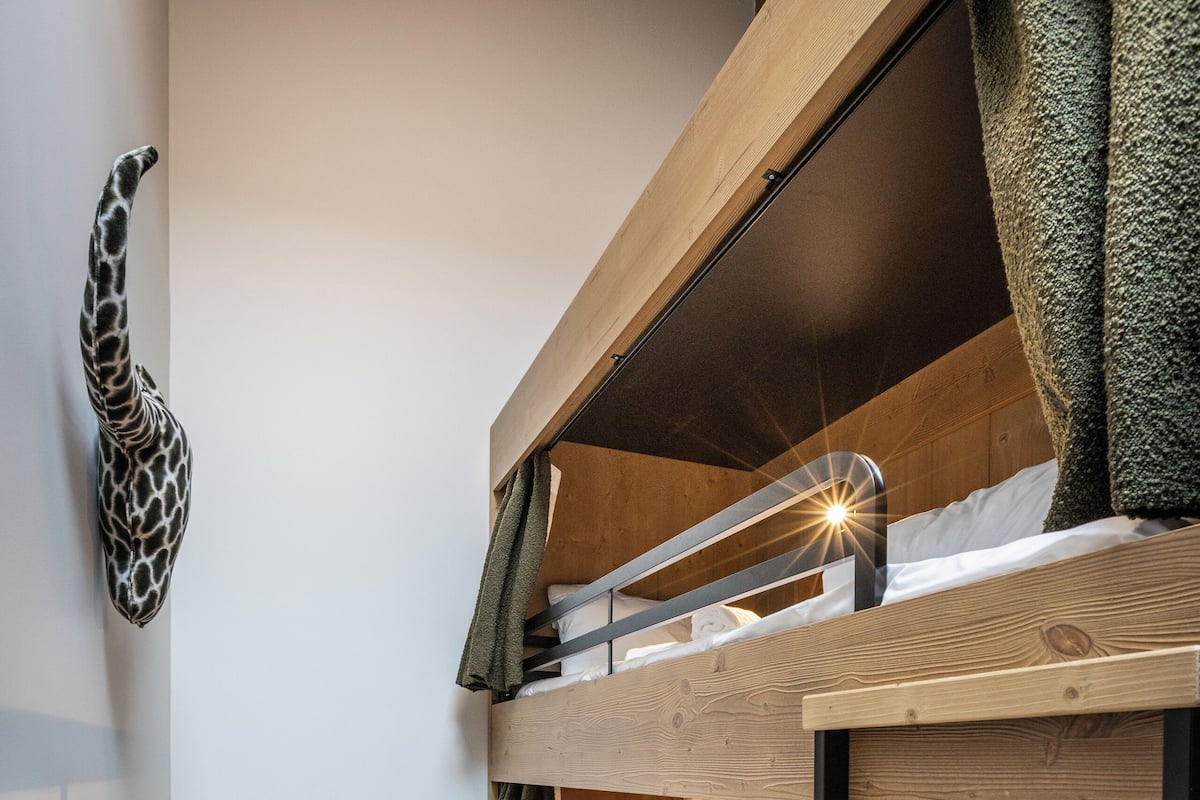 A bunk bed room with a giraffe head decoration, wooden flooring, and a small table.