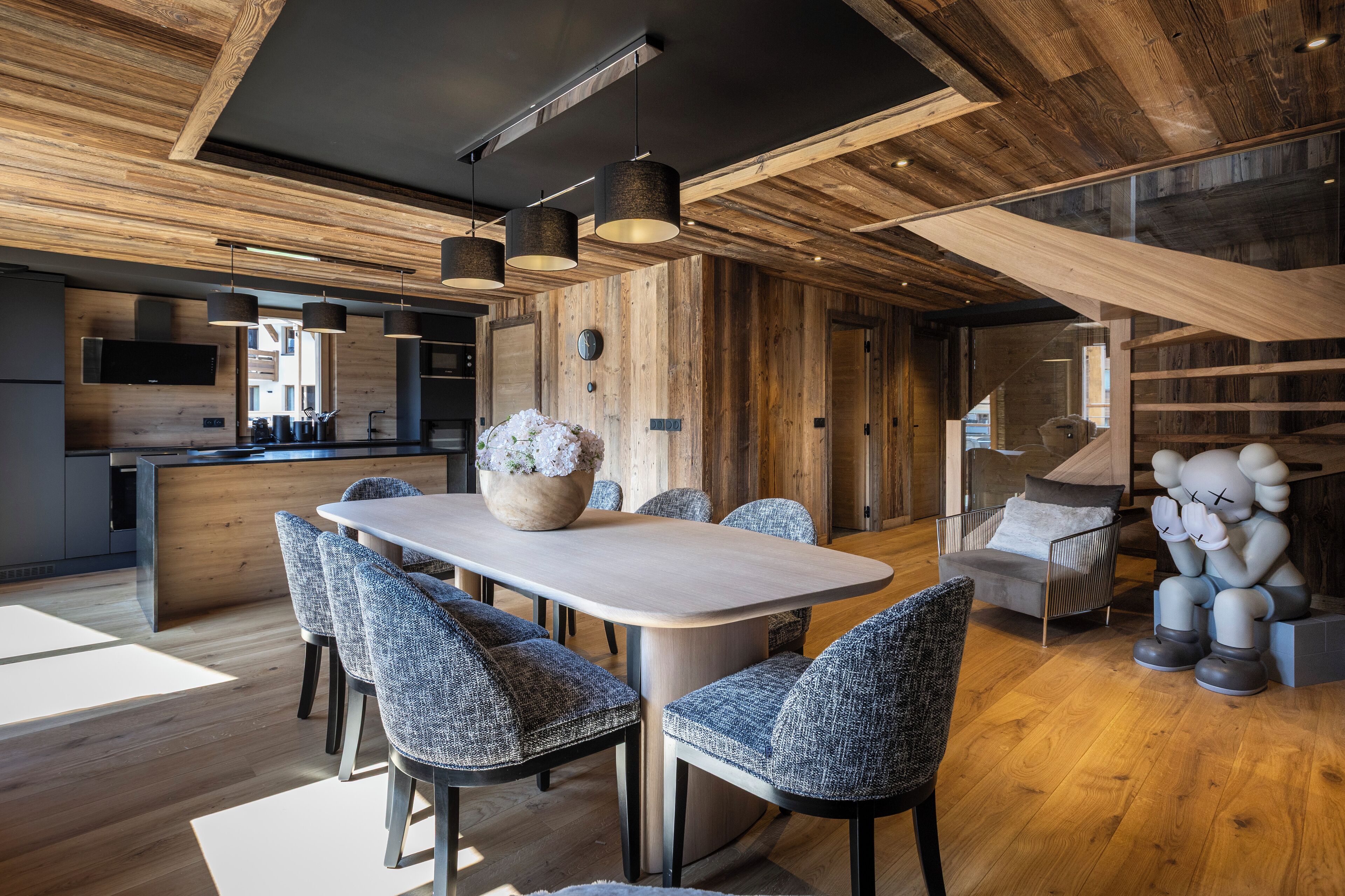 A modern kitchen with wooden accents, a dining area with a large table and chairs, and a staircase with a unique design.