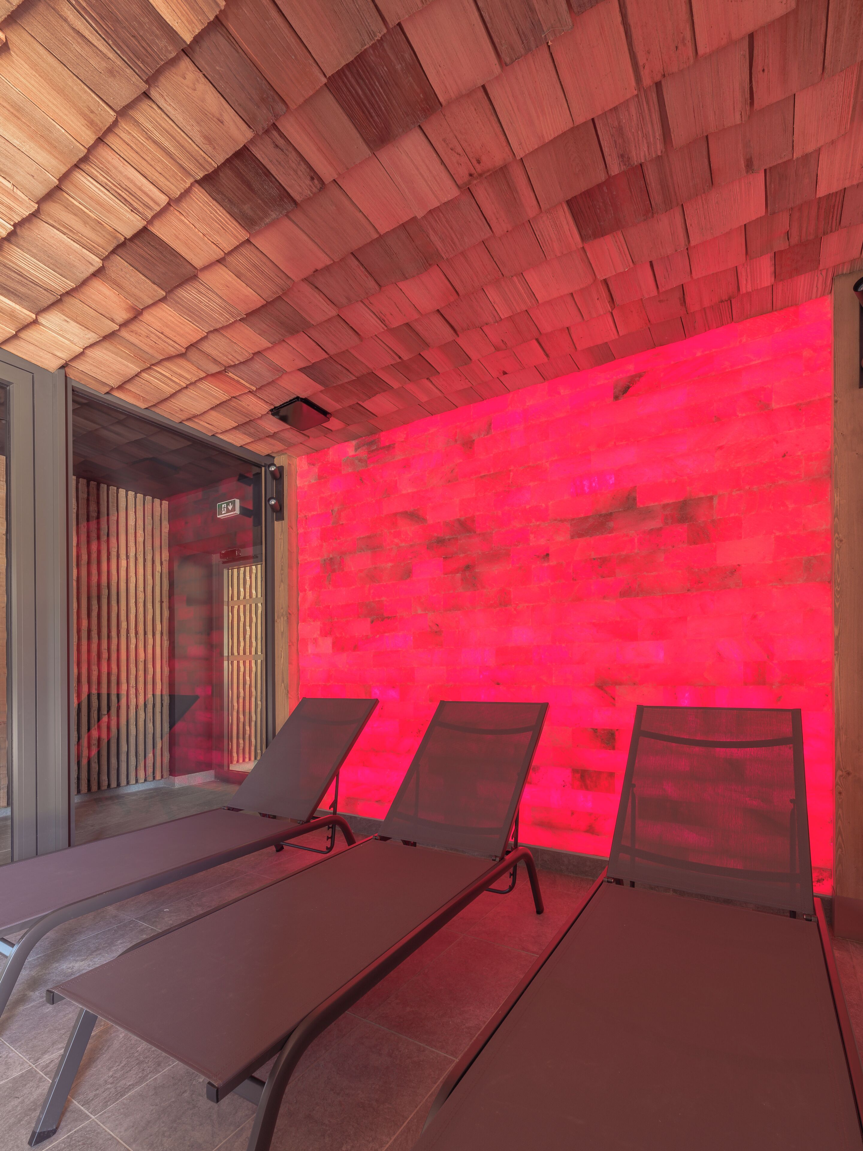 A room with three sun loungers, a wooden ceiling, and a red wall.