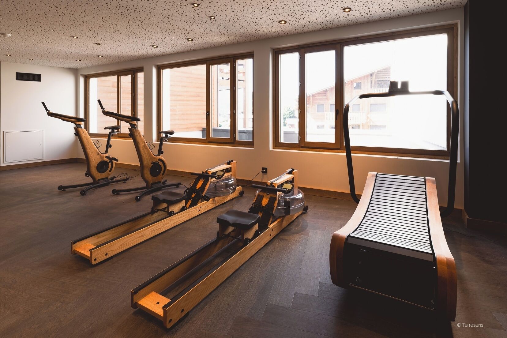 A gym with exercise equipment, large windows, and a wooden floor.