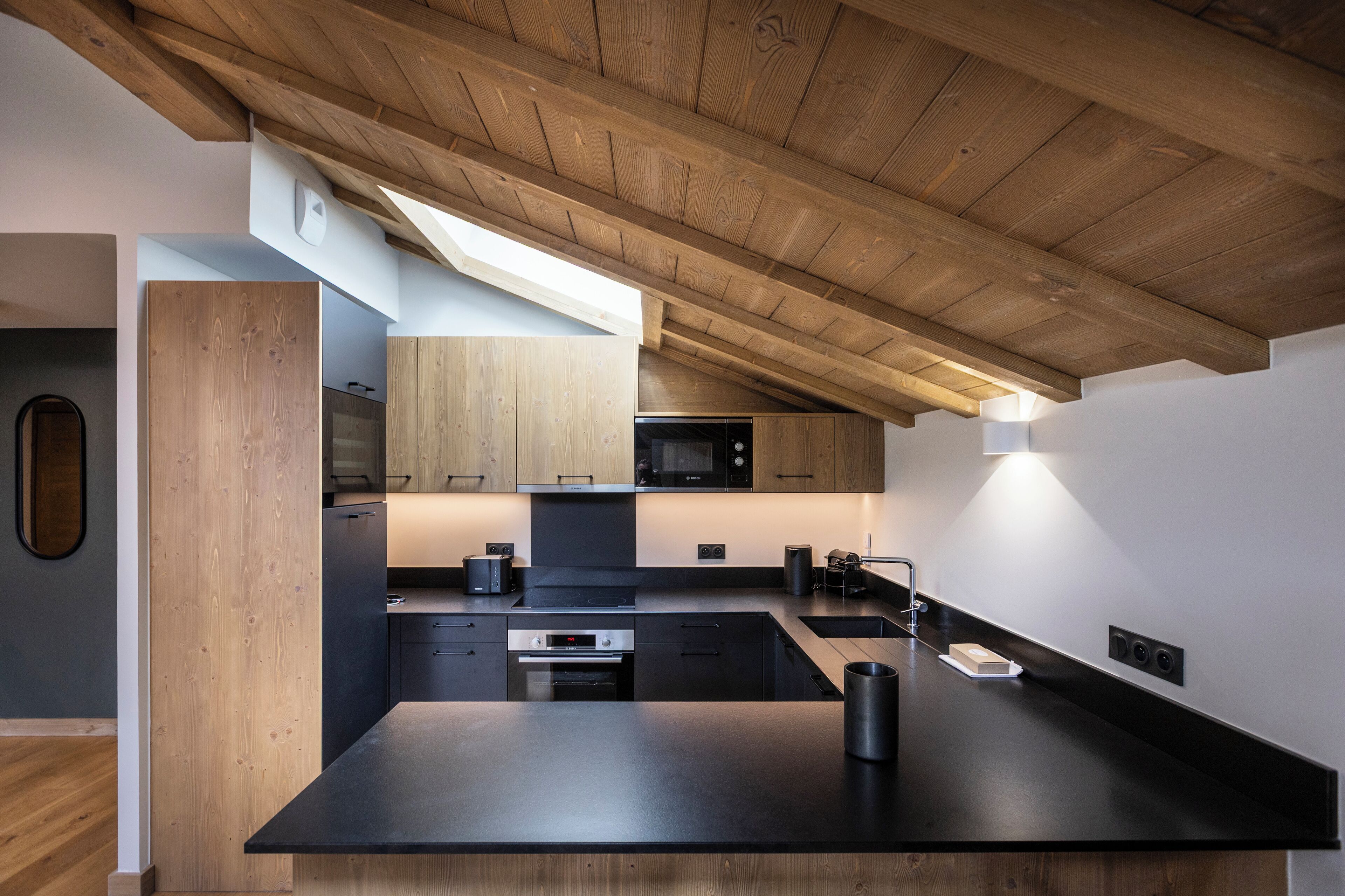A modern kitchen with wooden beams, built-in appliances, and a sleek black countertop.