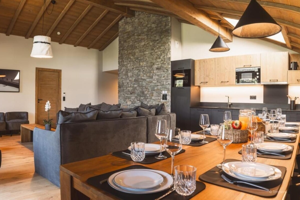 A modern kitchen with a stone accent wall, wooden cabinets, and a dining area set for six with a long table and six chairs.