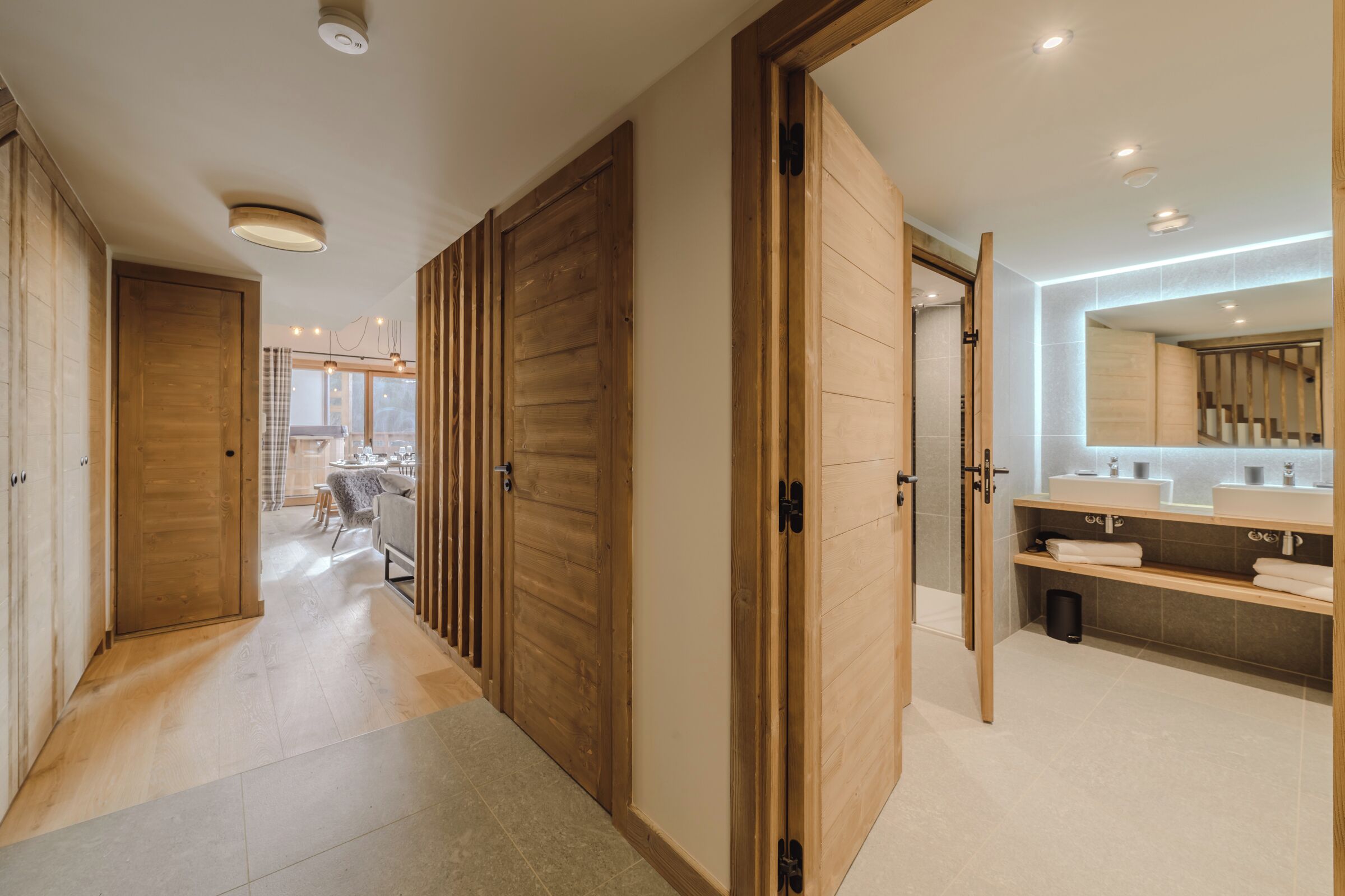 Une salle de bain moderne avec des portes en bois, un grand miroir et un meuble-lavabo doté de deux vasques.
