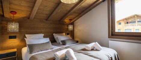 Un dormitorio acogedor con vigas de madera, dos camas con toallas y un ventanal con vistas a un edificio.