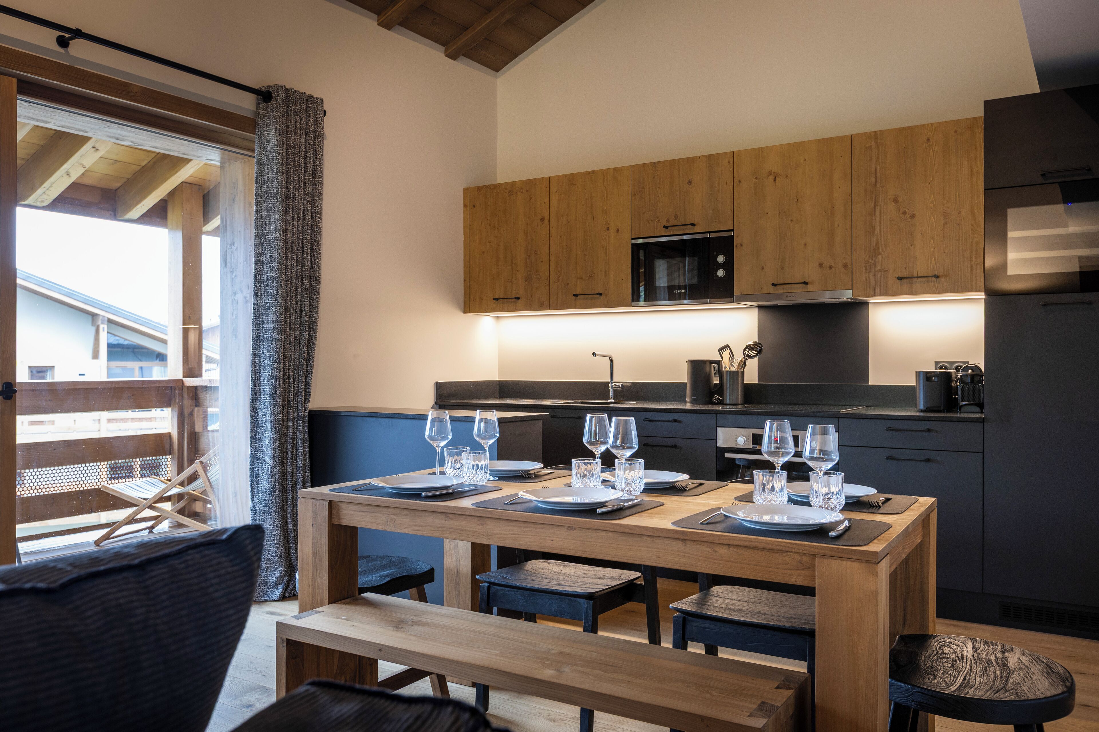 Una cocina moderna con armarios de madera, una mesa de comedor para cuatro personas y vistas al balcón exterior.