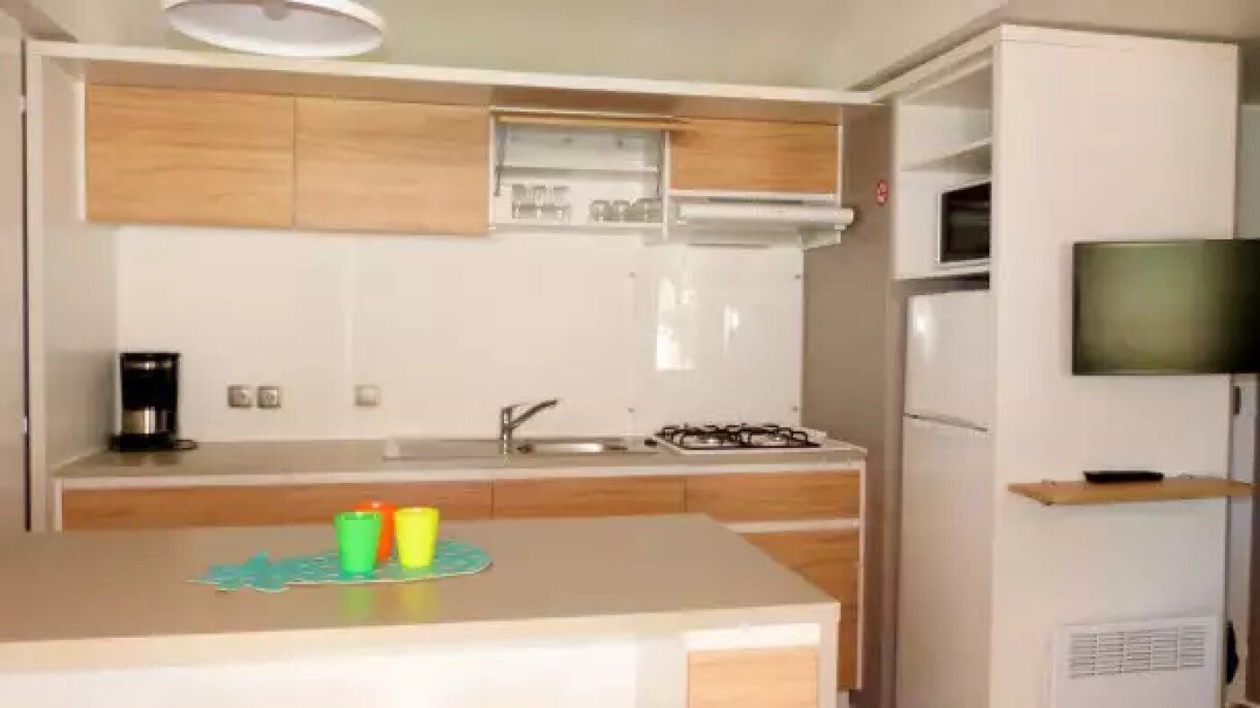 A compact kitchen with wooden cabinets, a gas stove, a microwave, and a small TV on a shelf.
