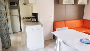 Cocina compacta con microondas, cafetera y refrigerador. En la sala de estar, hay un sofá naranja y una mesa blanca.