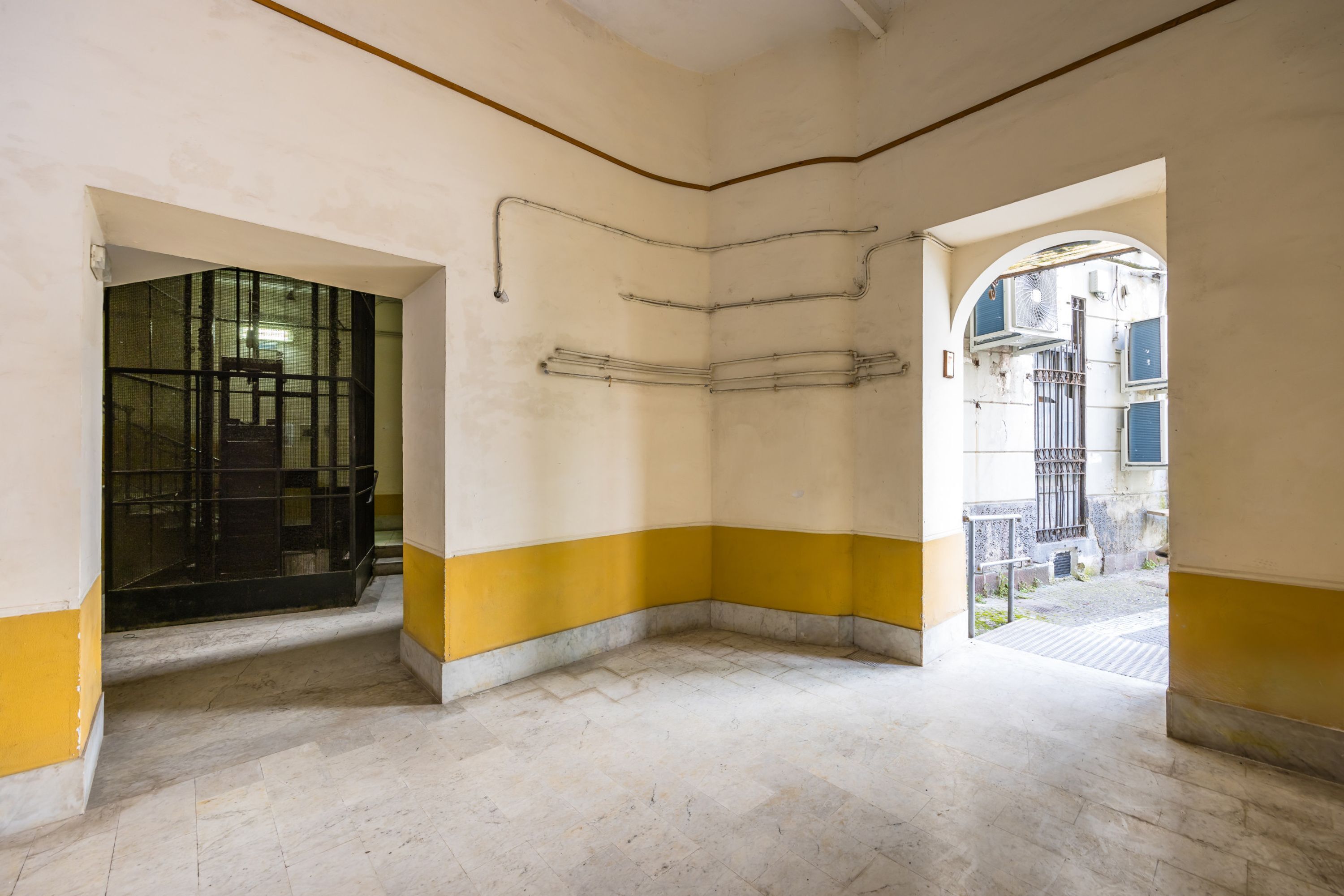 A room with a tiled floor, a yellow and white wall, and a doorway leading outside.