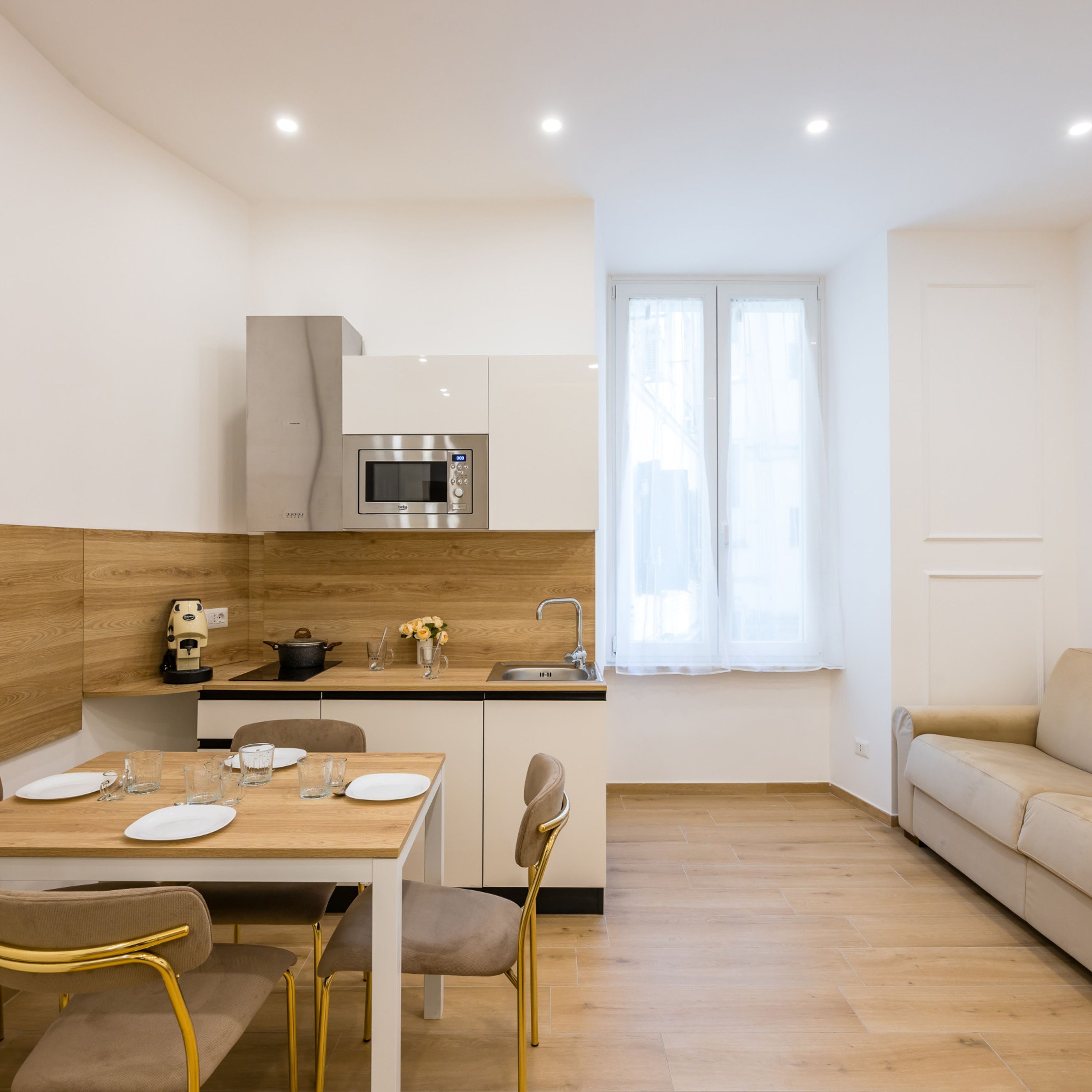 Una cocina moderna con microondas, lavamanos y encimera de madera. Hay una mesa de comedor con sillas y un sofá en la zona de estar.