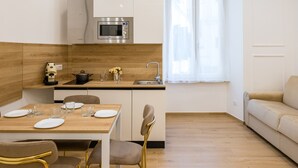 Eine moderne Küche mit Mikrowelle, Spüle und Holzarbeitsplatte. Im Wohnbereich steht ein Esstisch mit Stühlen sowie eine Couch.