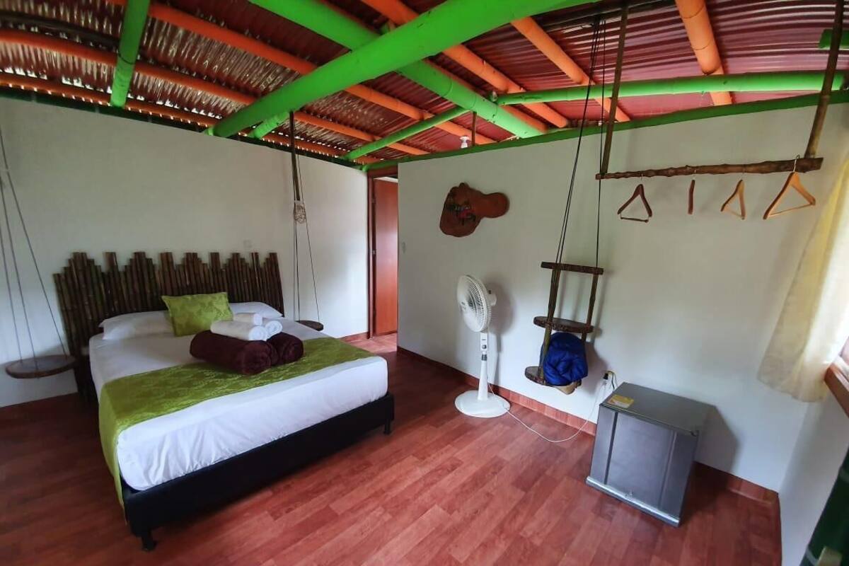 A bedroom with a bed, a fan, a small cabinet, and a wooden headboard.