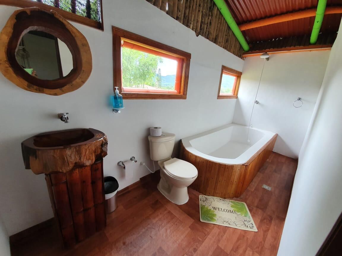 Une salle de bain avec un meuble-lavabo en bois, des toilettes, une baignoire et deux fenêtres.