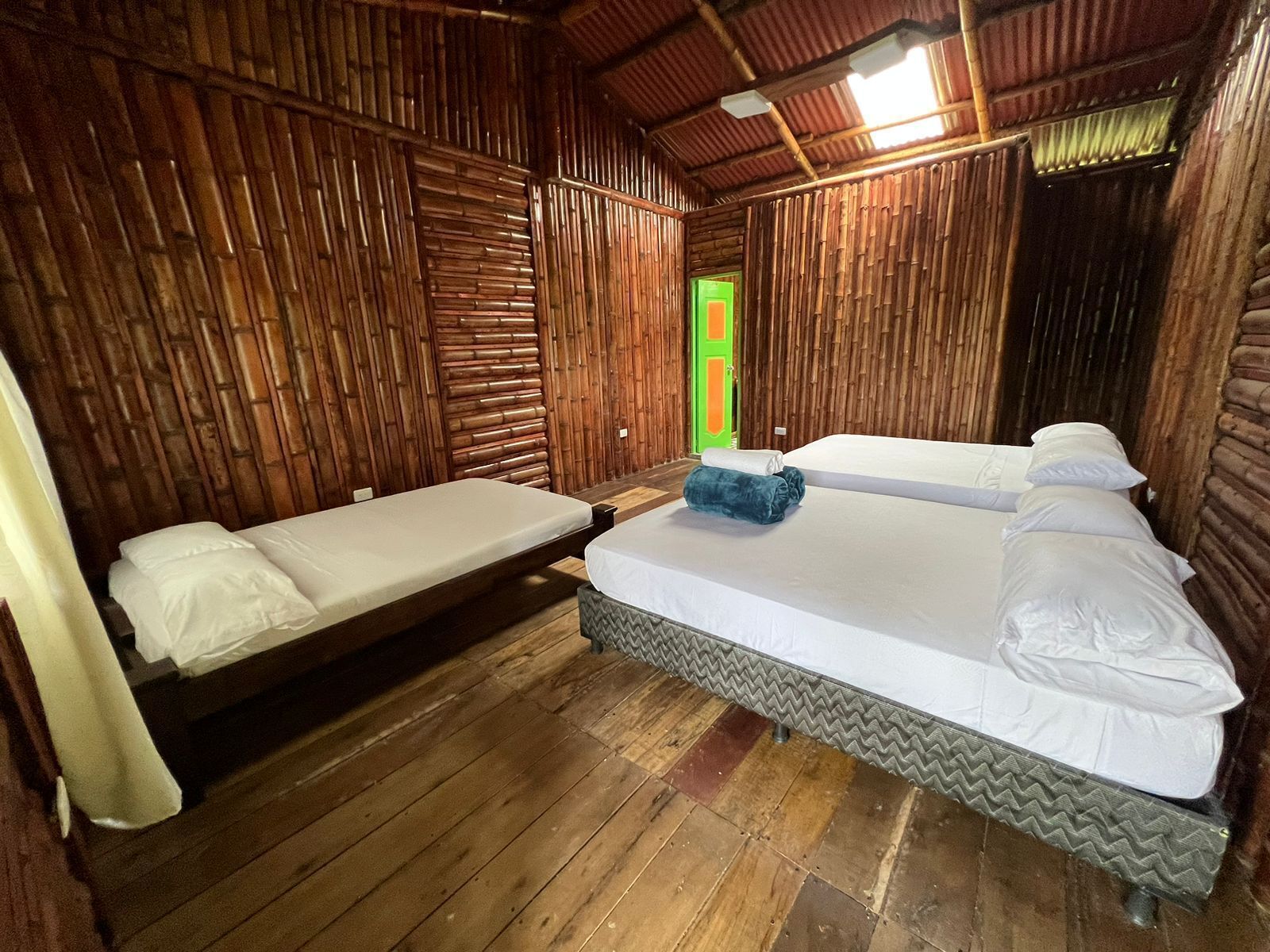 A room with two beds, wooden walls, a green door, and a tiled floor.