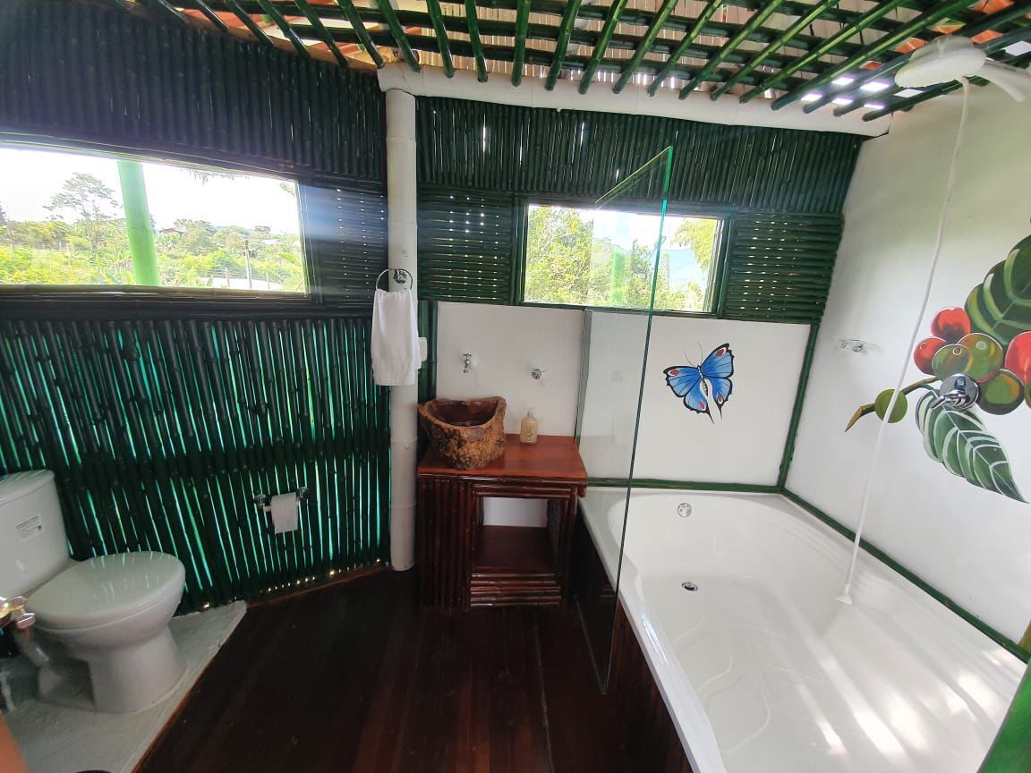 A bathroom with a toilet, a sink, and a bathtub. There is a window with blinds, a mirror, and a wall with a butterfly and fruit mural.
