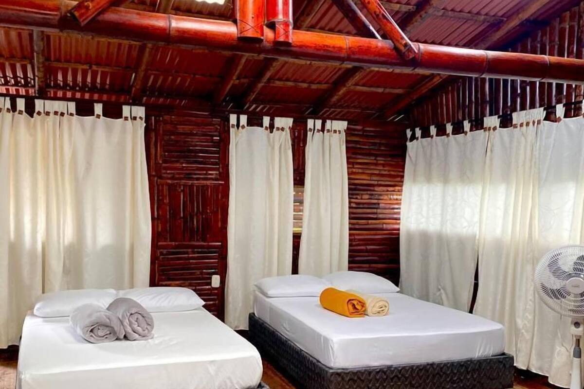 A room with two beds, wooden flooring, and a ceiling with exposed pipes.