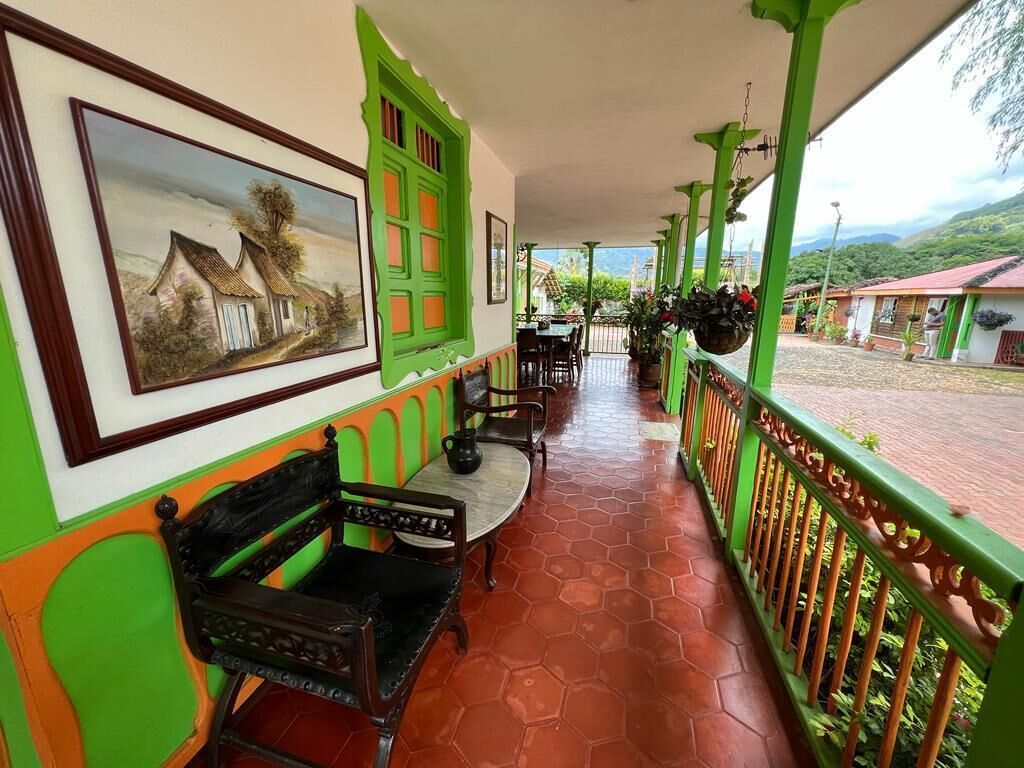 A covered outdoor area with a green railing, a bench, a table with chairs, and a hanging planter.