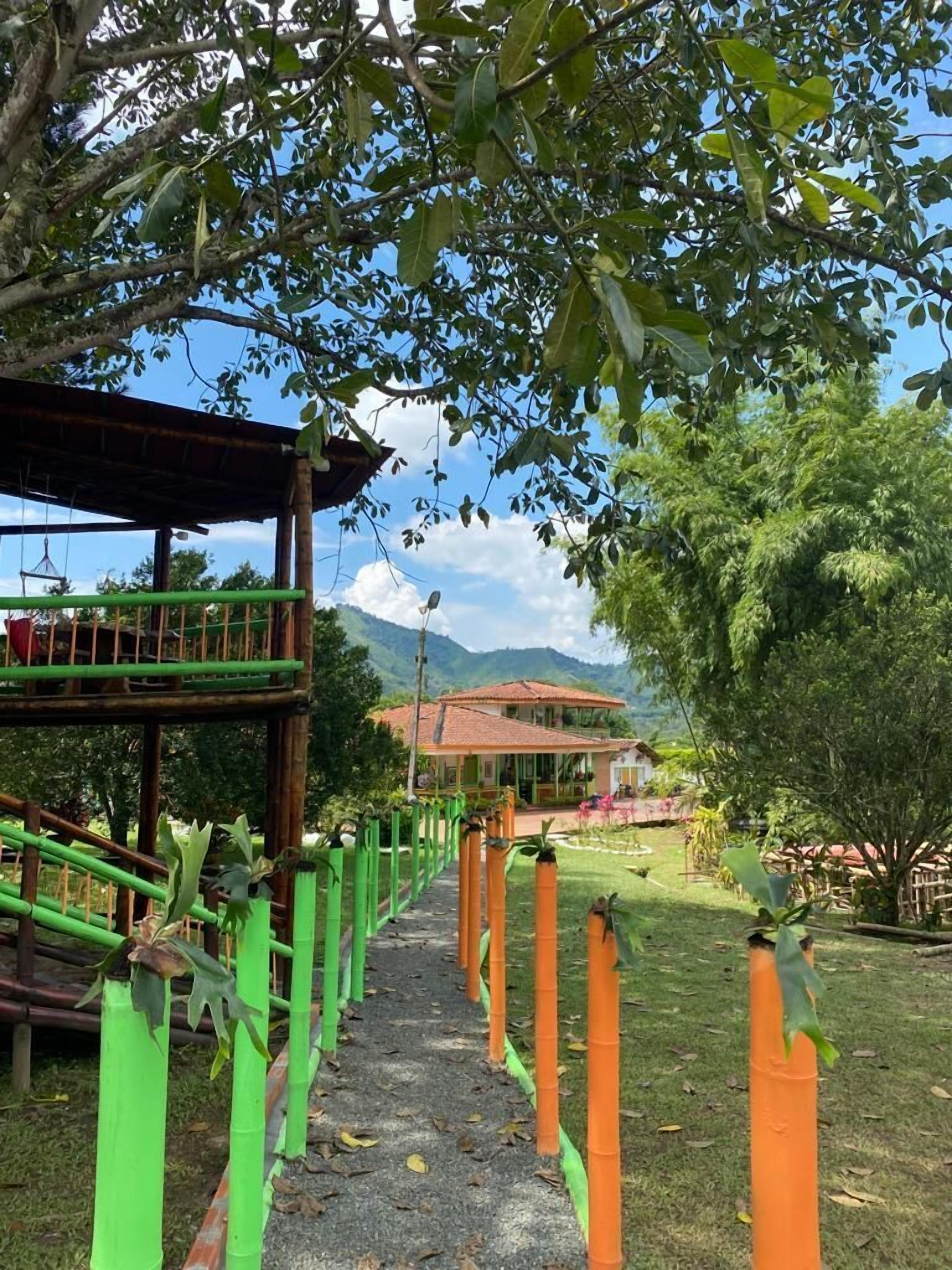 Un sendero lleva a una casa con techo de tejas rojas, rodeada de abundante vegetación y árboles.