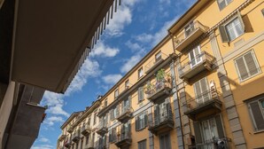 A multi-story building with balconies, parked cars, and a clear sky.