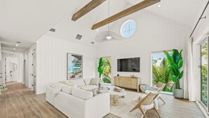 A spacious living room with a white sofa, a coffee table, and a TV. There are large windows and a view of greenery outside. - Experience Luxury at Go with the Flow! Lazy River Pool, Rooftop Deck and Games! (Anna Maria)