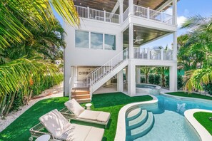 A modern two-story house with a pool, outdoor seating, and lush greenery. - Experience Luxury at Go with the Flow! Lazy River Pool, Rooftop Deck and Games! (Anna Maria)