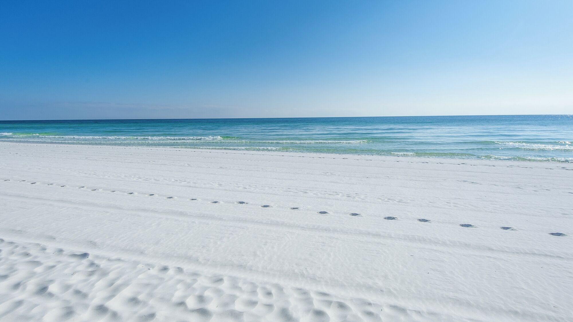 A beach with white sand and clear blue water.