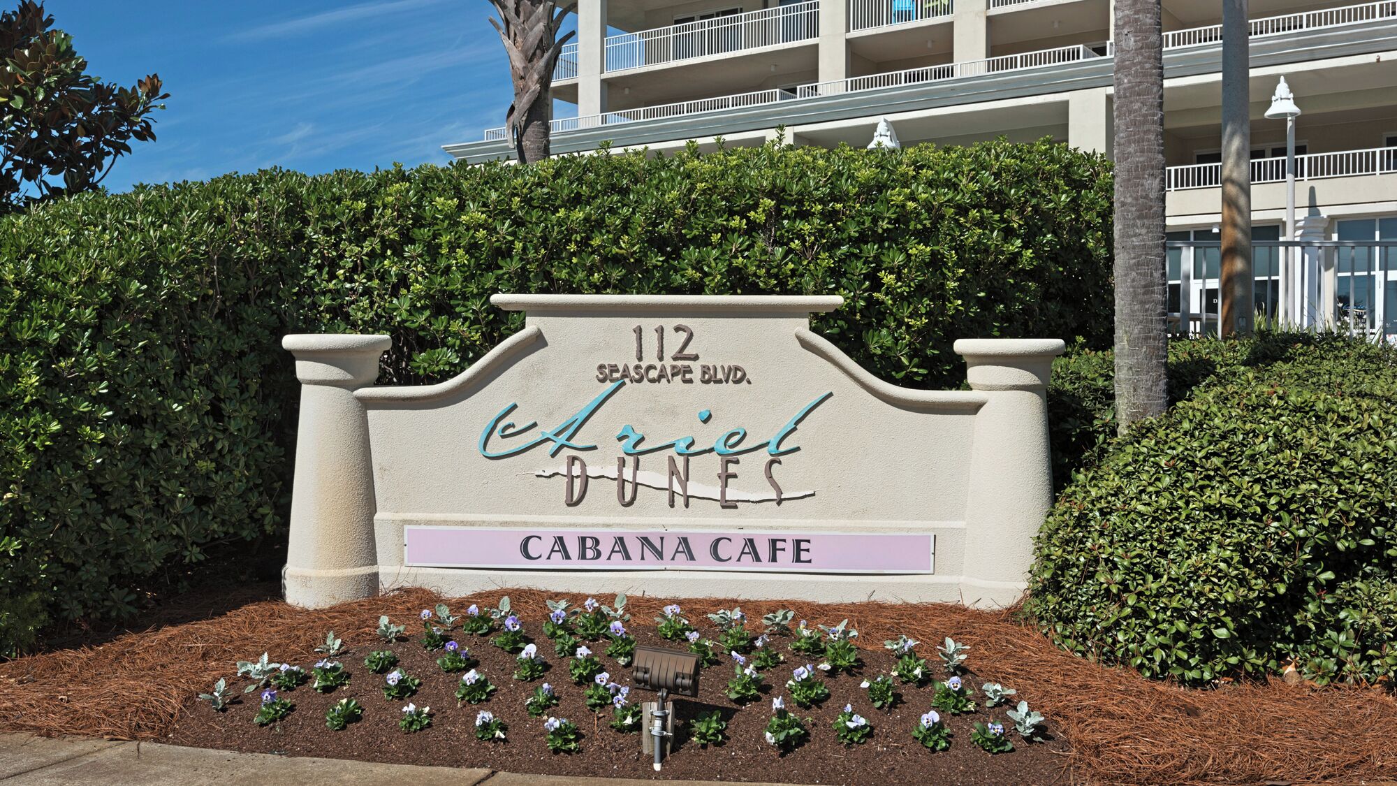 A sign for 'Cabana Cafe' at 112 Seascape Blvd. with a landscaped area in front.