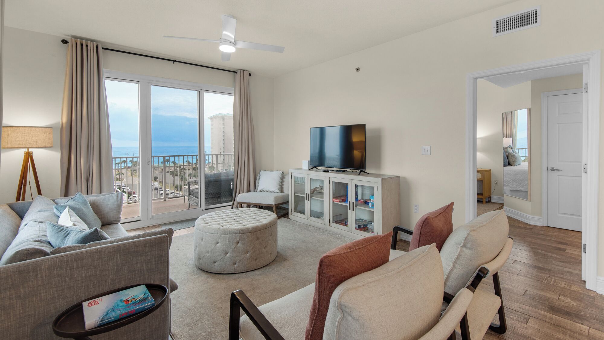 Een ruime woonkamer met een groot raam, een flatscreen televisie en een balkon met uitzicht op de oceaan.