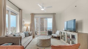 Uma sala de estar moderna com um sofá, um banquinho e uma televisão sobre um móvel.