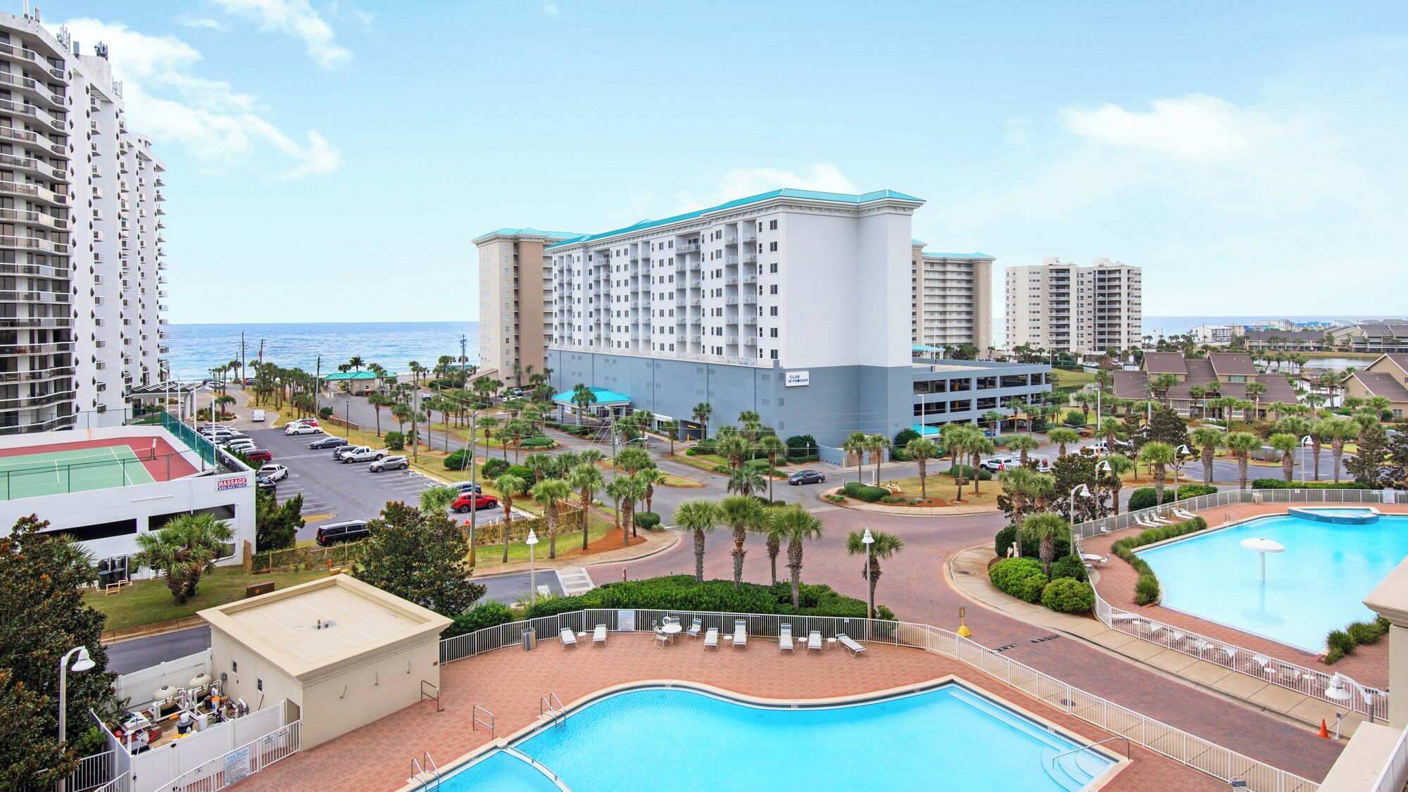 A resort with a large pool, multiple buildings, and a view of the ocean.