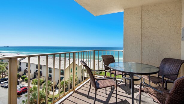 Ein Balkon mit Glastisch und Korbstühlen mit Blick auf einen Strand.